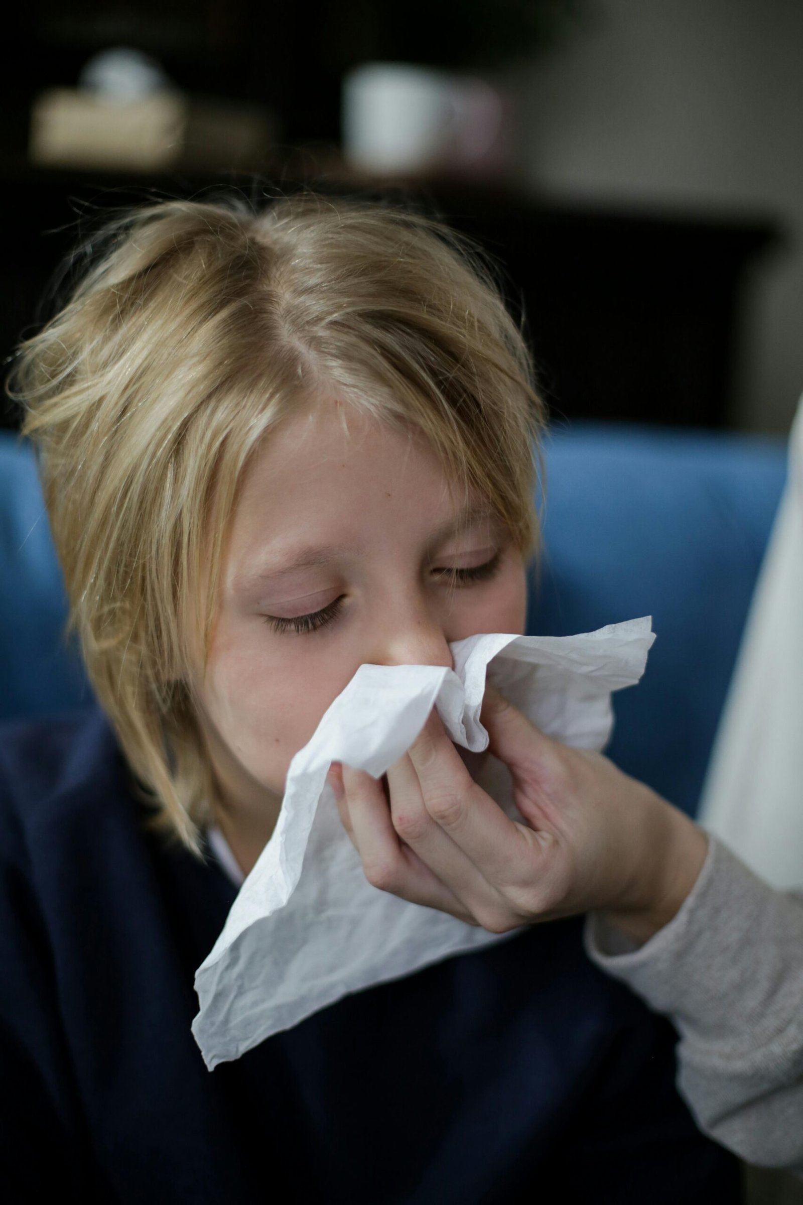 Young girl sneezing into a tissue while being comforted. Indoor setting.
