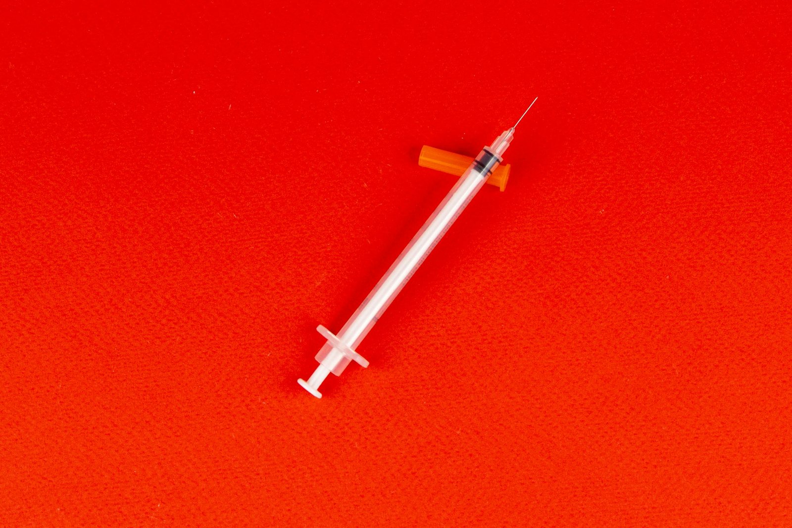 A syringe lying on a vivid red background, captured from above, signifying medical themes.